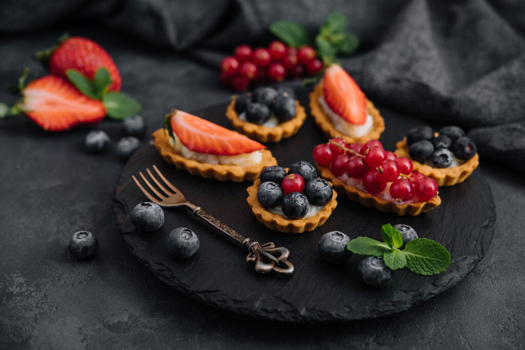 Delicious tartlets with fruit and cream mascaropne on black board
