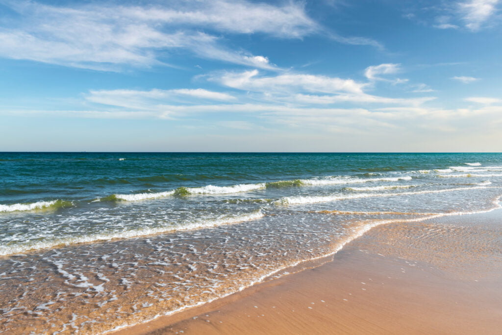 Tide waves on tropical beach sand and blue ocean