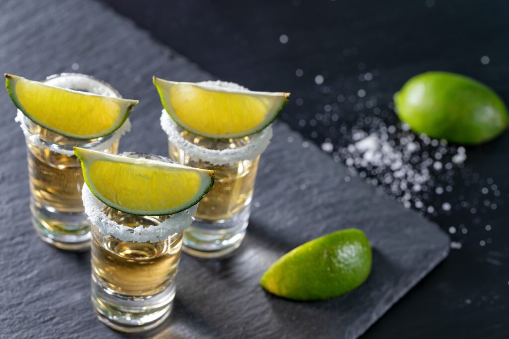 Three glasses of mexican tequila and lime on dark background